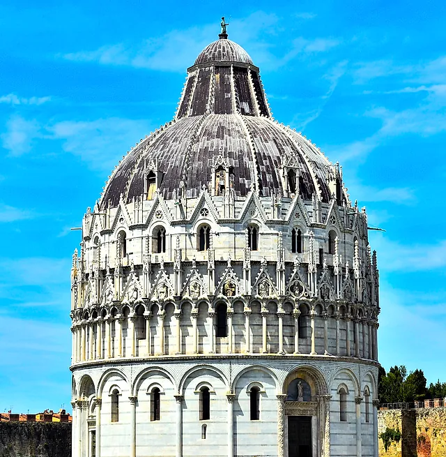 Il Battistero di Pisa, un edificio rotondo di marmo bianco con la cupola a coste e i pinnacoli gotici, contro un cielo azzurro intenso