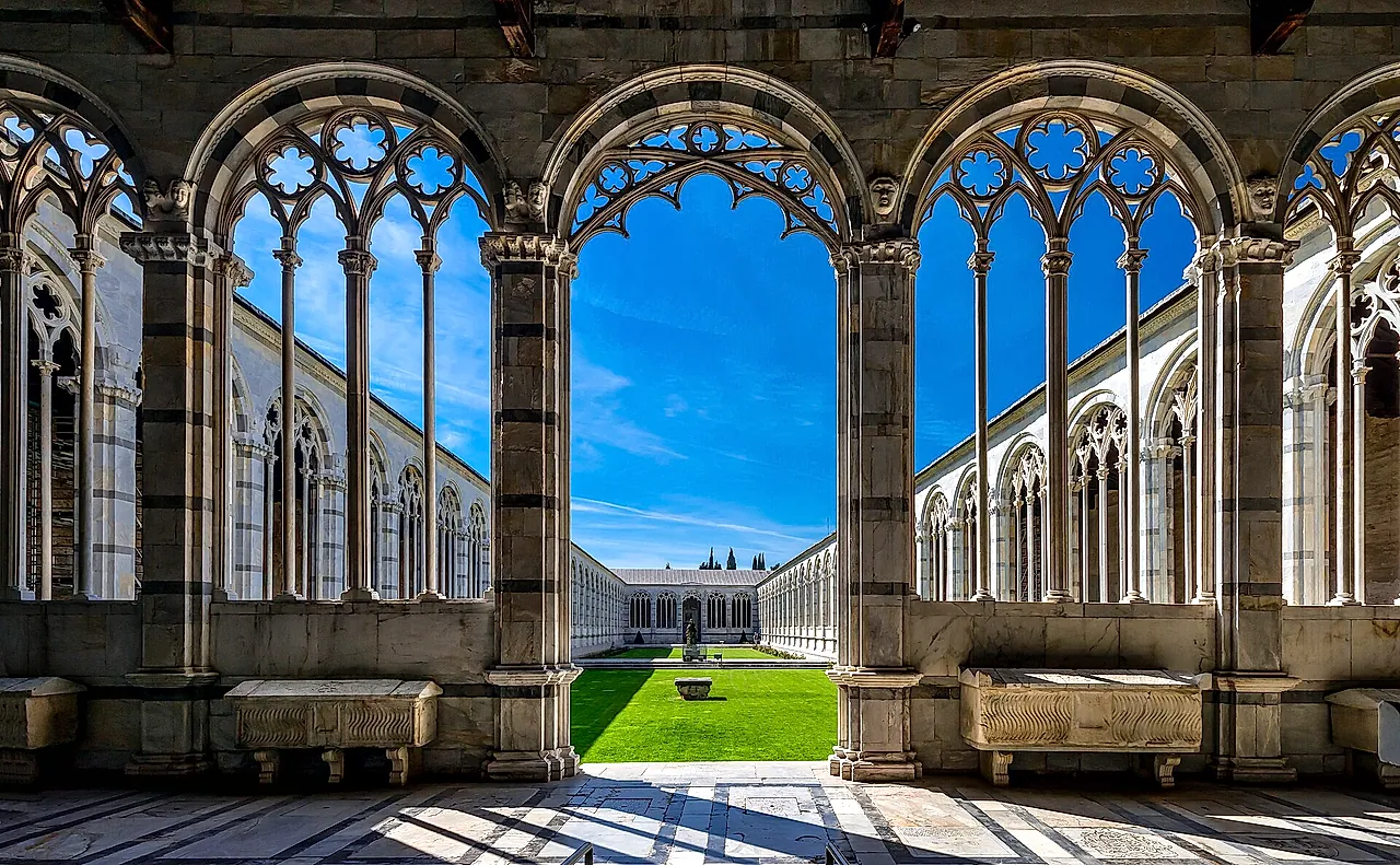 Gli archi gotici del Camposanto Monumentale che incorniciano il cortile verde al sole
