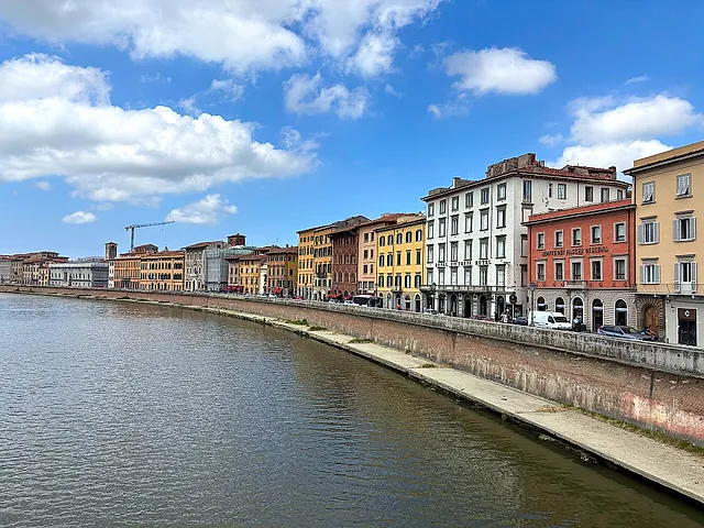 Il Lungarno di Pisa: l'Arno che curva lungo una fila di palazzi dai colori pastello sotto un cielo con nuvole