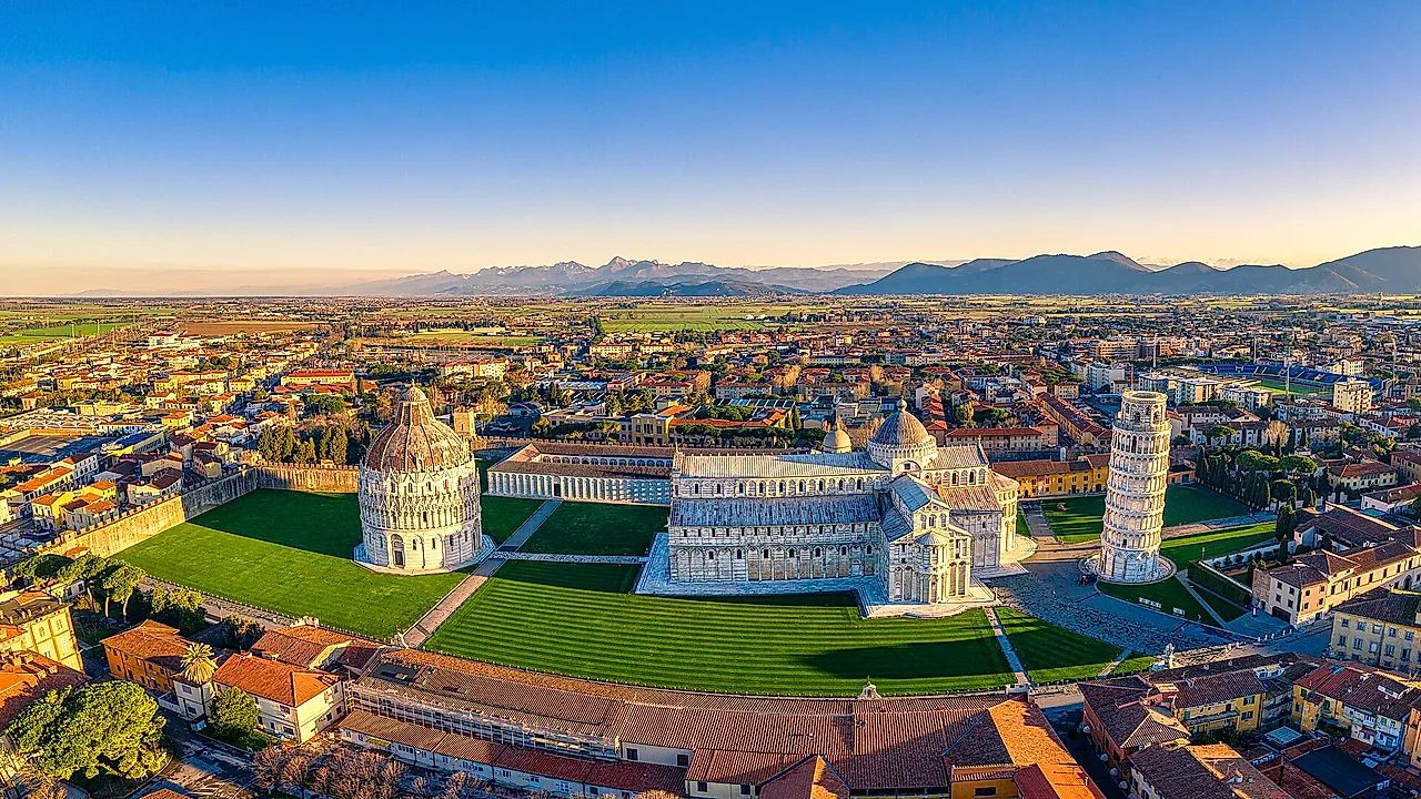 Veduta aerea di Piazza dei Miracoli: il Battistero, la Cattedrale e la Torre pendente sul loro prato verde, con i tetti di Pisa e le colline sullo sfondo