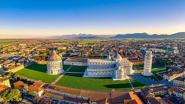 Veduta aerea di Piazza dei Miracoli: il Battistero, la Cattedrale e la Torre pendente sul loro prato verde, con i tetti di Pisa e le colline sullo sfondo