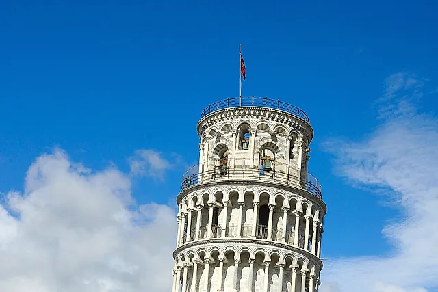 La Torre pendente di Pisa vista dal prato: i piani di colonne in marmo bianco inclinati contro un cielo azzurro con nuvole